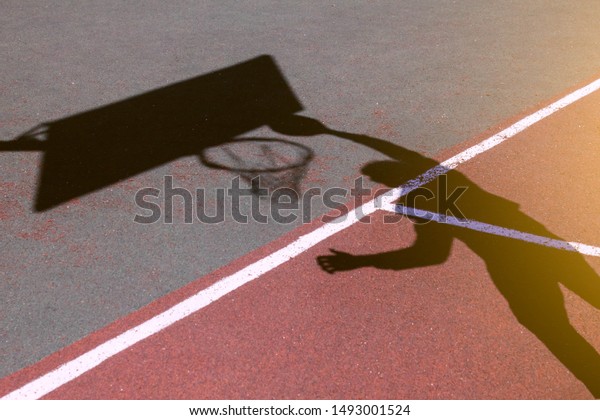 バスケットボールでダンクをする男の影がバスケットにジャンプする スポーツとバスケットボール バスケットボールの選手のシルエット プレイグラウンドの表面に 影を落とす バスケットボールのコンセプト の写真素材 今すぐ編集
