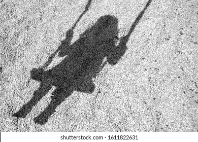 A shadow on the ground with stones of a kid on a child swing under sunlight - Powered by Shutterstock