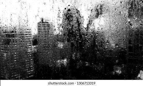 Shadow of oneself looking to a wet and misery day through raindrops-covered window. High contrast black and white image.  - Shutterstock ID 1306713319