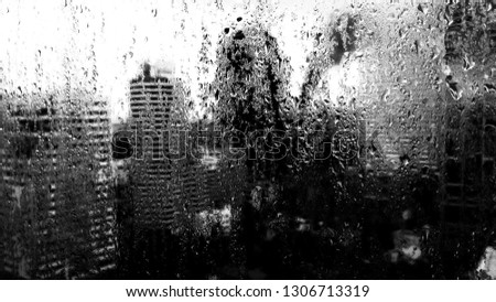 Shadow of oneself looking to a wet and misery day through raindrops-covered window. High contrast black and white image. 