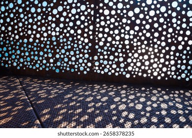Shadow pattern of round perforations on a metal wall with ocean view in the background.