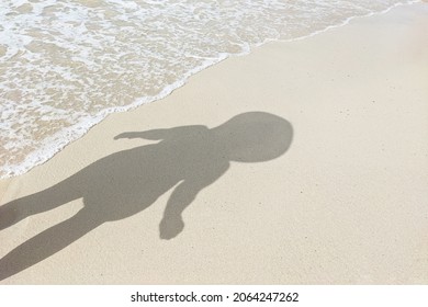 Shadow Of A Person With Big Head On The Beach Sand With Sea Waves. Concept Of Aliens, Humanoids, Underwater Inhabitants