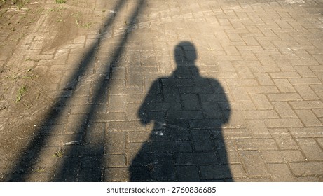 Shadow of person standing on patterned brick pavement with sunlight casting silhouette and textures.