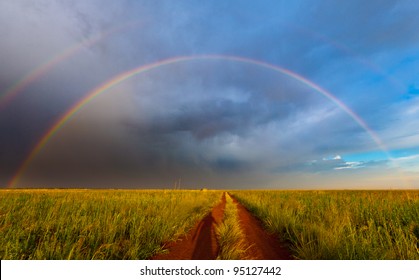 A shadow of the photographer is cast onto a road, leading towards an epic double rainbow sunset - Powered by Shutterstock