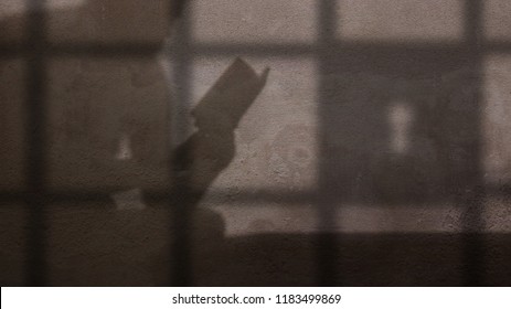 Shadow Of Prisoner Reading A Book Behind Jail Bars