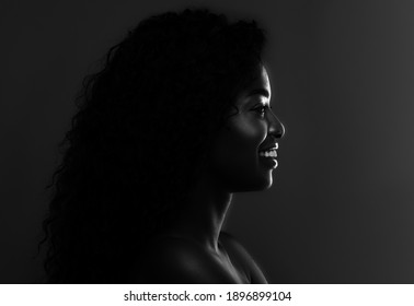 In The Shadow. Profile Portrait Of Black Attractive Female Posing Over Dark Background, Monochrome Shot Of Young Smiling African American Woman With Backlit, Bw Image, Side View With Copy Space