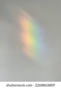 Shadow of rainbow on the white wall. Colourful background. Reflection of the sun on the white background. Blurry. Selective focus.