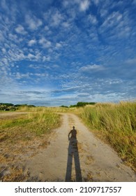 Shadow Of A Runner Against Blue Sky And Open Green Field