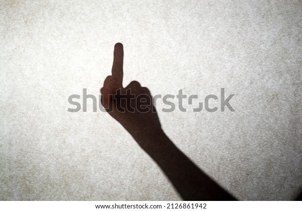 Shadow\
silhouette of a human hand on a wall. fuck sign. A rude gesture of\
the middle finger raised up denoting\
anger