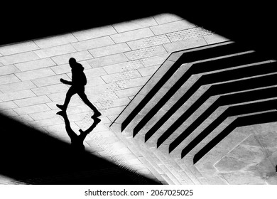 Shadow Silhouette Of Teenage Boy Walking City Street Sidewalk, In Black And White From Above