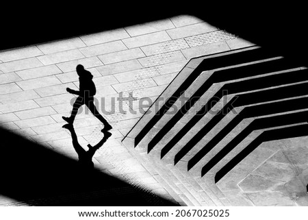 Shadow silhouette of teenage boy walking city street sidewalk, in black and white from above