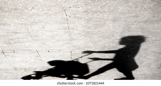 Shadow Silhouette Of A Young Woman Pushing A Baby Stroller On City Sidewalk In Black And White