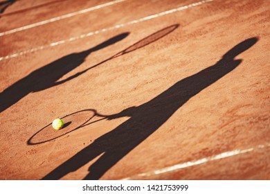 Shadow of a tennis ball and tennis player in action on a clay court .