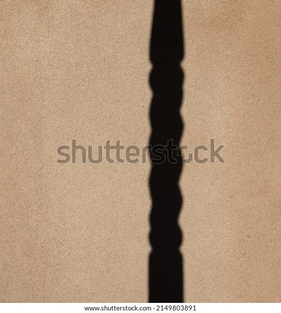 shadow of turned column cast onto textured outdoor\
exterior beige cement plaster or concrete home wall vertical format\
room for type vertical beige and black backdrop background or\
wallpaper 