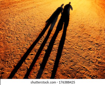 Shadow Of Two People Holding Hands Walking Down A Dirt Road Together