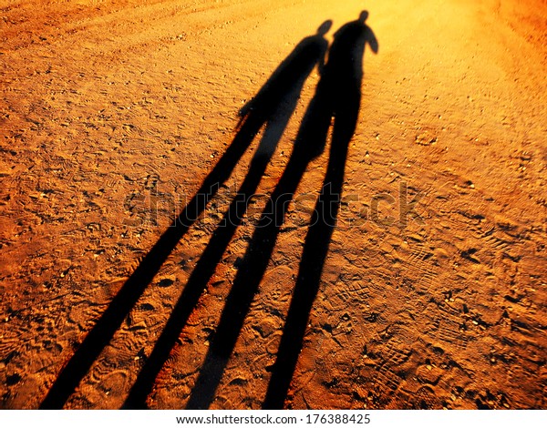 Shadow Of Two People Holding Hands Walking Down A Dirt Road Together