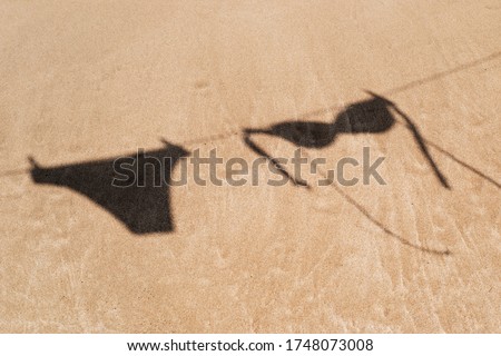 the shadow of the two pieces of a bikini hanging on a clothes line on the sand of a beach
