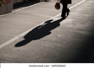 Shadow of unrecognizable businesswoman carrying a handbag on a deserted city street
