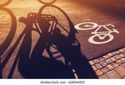 Shadow of unrecognizable cyclist riding a bike on bicycle lane through city street next to the road marking in urban surrounding, retro toned - Powered by Shutterstock