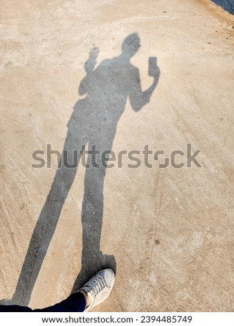 Shadow of a woman on the road. Woman holding a glass of water with her left hand and holding the phone with his right hand, standing with his back to the sun, causing a shadow to appear. Funny shadow