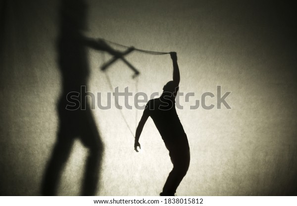 Shadow of woman silhouette holding a man like in a\
puppet show. Manipulation and dependence and control concept.\
Marriage and divorce idea. Debts and microcredits problem. Squid\
game idea. Copy space.