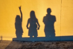 Shadows Of A Family Of Three People On The Wall At Sunset Time. Group Of Human Shadows On The Stone Wall Background.