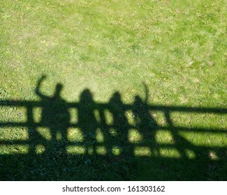Shadows of four people on grass pavement.People shadows on the bridge, artistic photo with selective focus. Contrast, people shadows on sunny day on grass background, abstract photo.Meeting of friends