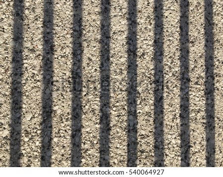 Shadows of jail cell bars in the prison camp on stones cement floor.