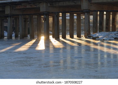 Shadows And Light From The Pillars Under The Bridge In Winter On The Ice Of The River.