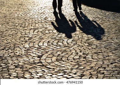 Shadows On Pavement Of Two Men Walking Under Bright Sunlight