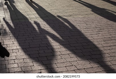 Shadows On Pavement Of Two People Walking Under Bright Sunlight.