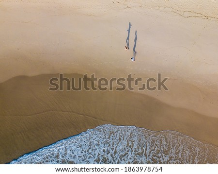Shadows running along a beach. The shadows are more distinct than the runners. A wave is running up the beach towards the runners