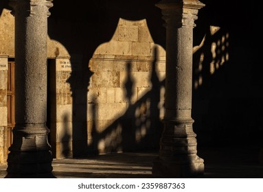Shadows and silhouettes of the arches, columns and granite fence of the cloister of the University of Salamanca with their shadow projected on the wall of the hallway by the evening sunlight. Chiarosc