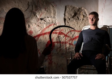 Shadowy Female Figure Holding Iron Sickle In Front Of Patient Near Blood Stained Wall For Concept About Murder And Scary Halloween Holiday