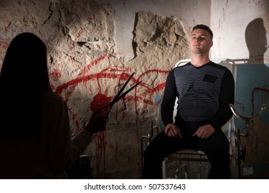 Shadowy Female Figure Holding Scissors  In Front Of Patient Near Blood Stained Wall For Concept About Murder And Scary Halloween Holiday