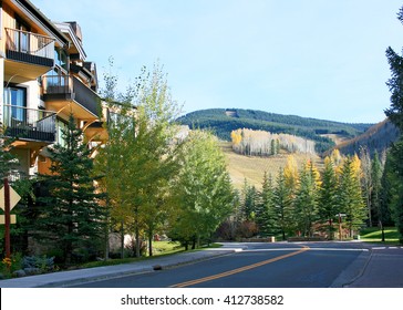 Shady Curving Street Along Building With Balconies And Mountain Landscape At Fall Time In Vail, Colorado