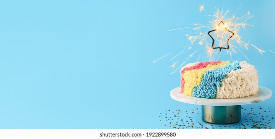 Shag cake with burned sparkler star on blue background. Colorful shag cake with perfect vanilla buttercream. Idea of visually striking cake decorating trendy cake, copy space. Long horizontal banner.