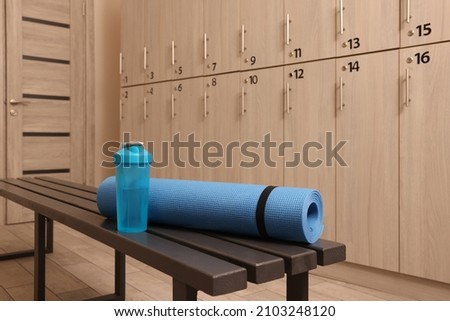 Shaker with water and yoga mat on wooden bench in locker room