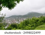 Shaki City in Azerbaijan sits nestled amidst rolling hills and abundant greenery, with clouds enveloping the landscape, creating a serene atmosphere.