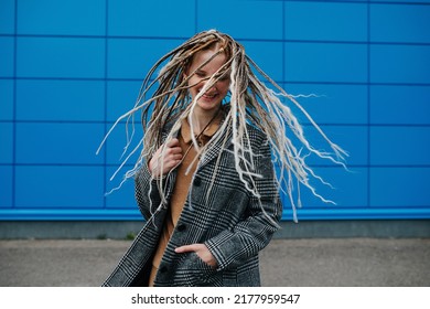 Shaking dreads lighthearted teenage girl in front of a blue panel wall covering. She is wearing a grey checkered jacket. Portrait. - Shutterstock ID 2177959547