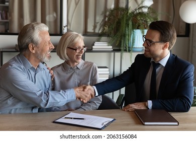 Shaking hands. Smiling young man real estate broker handshaking with older family couple after buying selling property. Spouses retirees thank bank agent for help after signing loan mortgage agreement