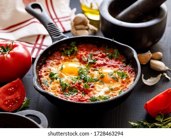 Shakshuka a traditional dish of eggs tomatoes and peppers with the addition of aromatic spices and fresh parsley in a cast iron skillet, close up