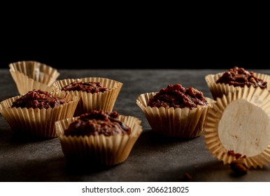 Shallow Depth Of Field Angled View Of Chocolate And Nut Muffins In Liner Papers Fresh Out Of Oven. Dark Background Moody Low Light Image. Crumbles On Stone Background