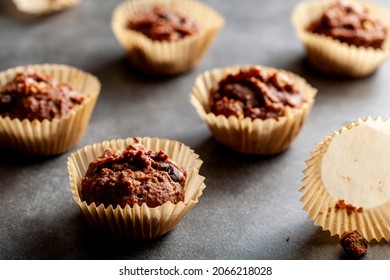 Shallow Depth Of Field Angled View Of Chocolate And Nut Muffins In Liner Papers Fresh Out Of Oven. Dark Background Moody Low Light Image. Crumbles On Stone Background