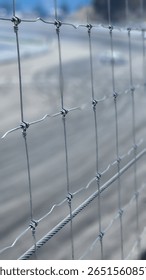 A shallow depth of field image featuring a tightly focused view of a metal fence at a racetrack. The blurred background shows tire marks and a drifting car in motion during a motorsport event.