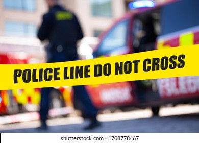 Shallow depth of field image of police tape with action of blurred police officer and emergency vehicles in the background. 