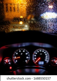 Shallow depth of field image (selective focus) with the steering wheel and dashboard lights of a 2010 car and the windscreen with drops of rain.