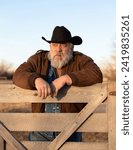 Shallow depth of field outdoor portrait of bearded old rancher cowboy focused on face while leaning on a fence looking to side in the distance in Yellowstone County Montana