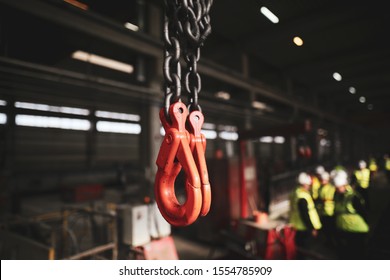 Shallow depth of field (selective focus) image with red industrial crane lifting hooks inside a factory.