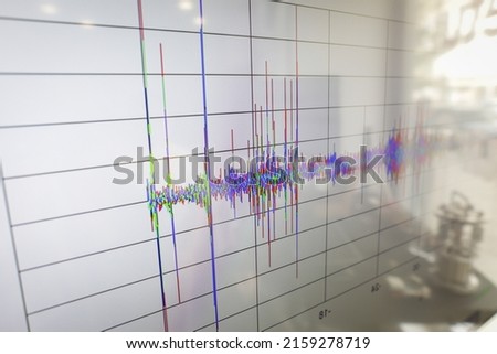 Shallow depth of field (selective focus) details with spikes on a seismogram on a digital display with the reflection of a device on the right.